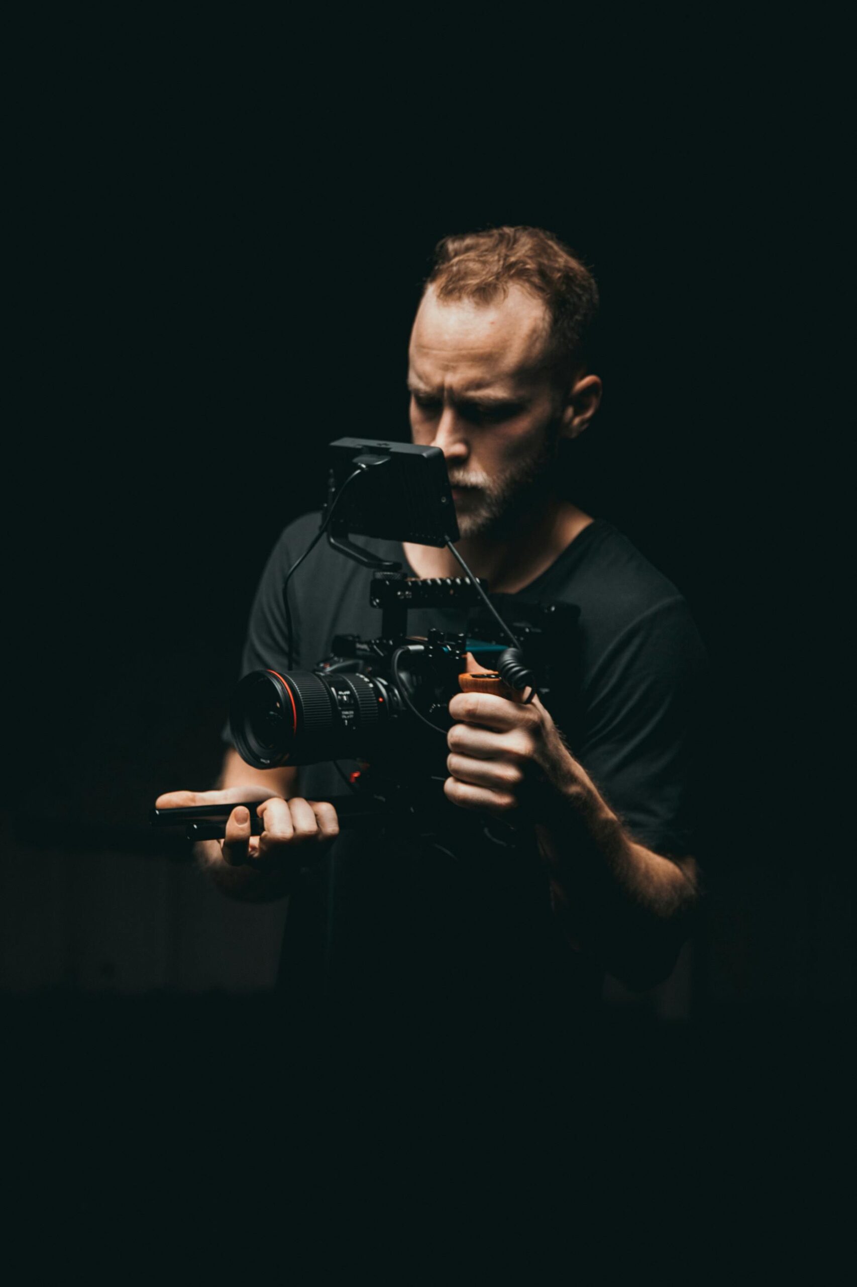 A focused cinematographer adjusts filming equipment on a dimly lit studio set, showcasing professional video production.