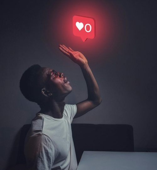 A man sits indoors reaching towards a glowing social media notification icon.